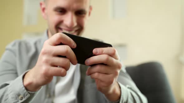 Happy, Young Man Playing Game on Smartphone at Home