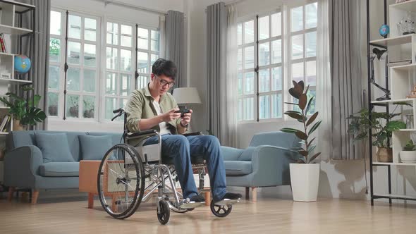 Asian Man Sitting In A Wheelchair While Use Mobile Phone Playing Video Game At Home