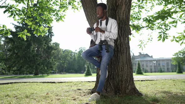 Wide Shot Happy Talented African American Photographer Standing at Tree Leaning on Trunk Watching