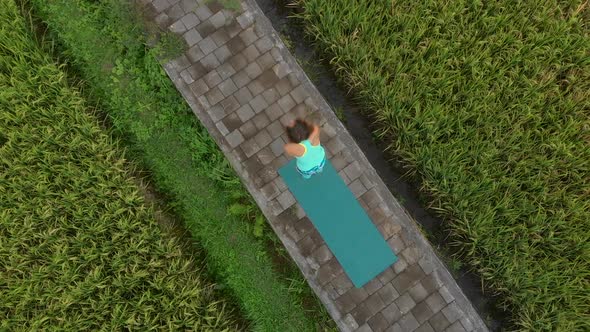 Aerial Slowmotion Shot of a Young Woman Practicing Yoga on a Beautiful Rice Field