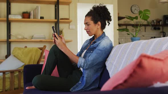 Caucasian woman using smartphone, sitting on sofa at home