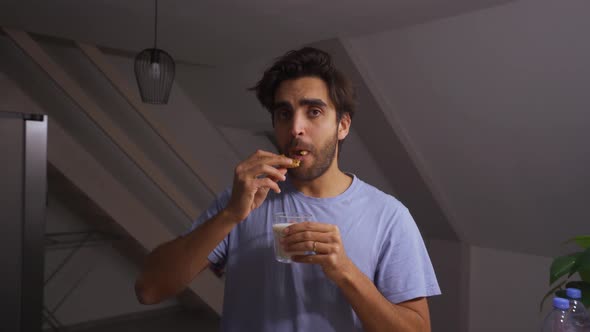 Man dipping a chocolate chip cookie in a glass of milk and eating it while making funny faces