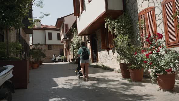 Woman Walks with Stroller on Narrow Street of Touristic Town