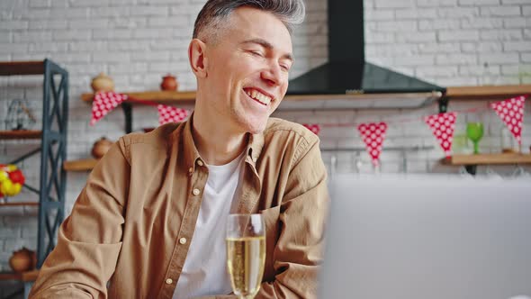 Happy Mature Man Sitting at Home and Drinking Champagne Celebrating Holiday Via Online Video Call on