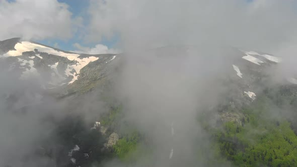 Aerial Forested Mountain With Snow Fragments Among The Clouds in The Spring