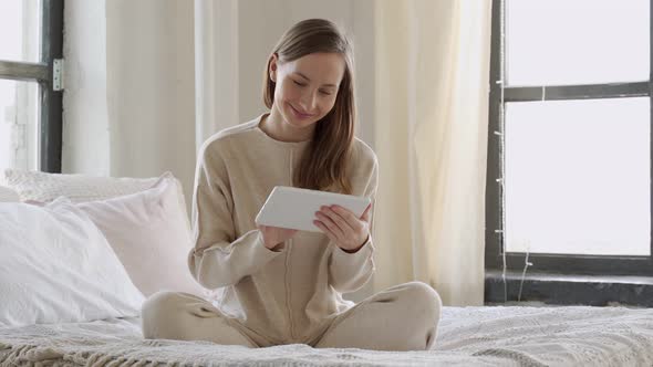 Young Woman Sits on the Bed and Using Digital Tablet