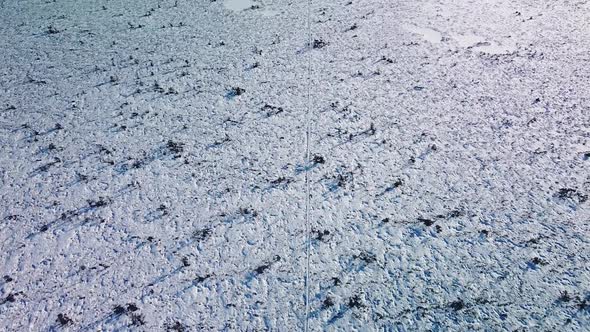 Revealing aerial view of snowy bog landscape with hiking trail and frozen lakes in sunny winter day,
