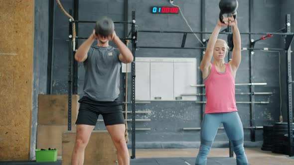 Girl and Guy Training with Kettlebells Squatting Lifting Weight Working Out Indoors Together