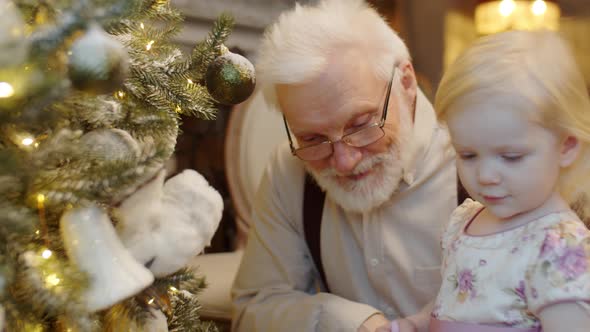 Cute Toddler Girl and Grandfather Decorating CHristmas Tree