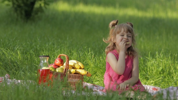 Weekend at Picnic. Caucasian Child Girl on Grass Meadow with Basket Full of Fruits. Eating Pancakes