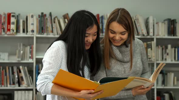 Two Female Students Compare Information in Two Books at the Library