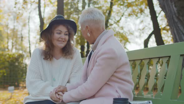 Happy Senior Mother and Daughter Sitting on Park Bench and Talking