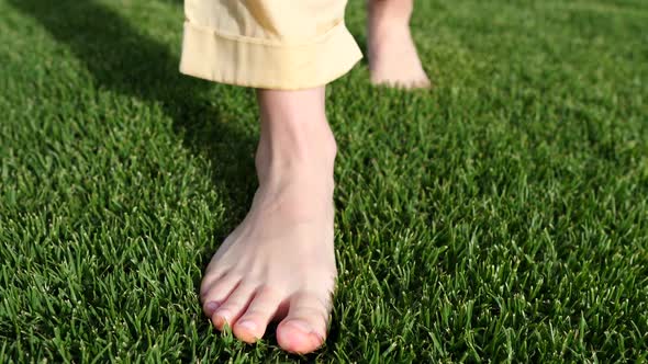 Female Legs Walking Barefoot On Green Grass. Closeup.