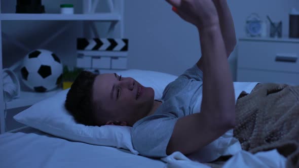 Teen Boy Making Selfie on Smartphone Putting It in Bed and Falling Asleep, Relax