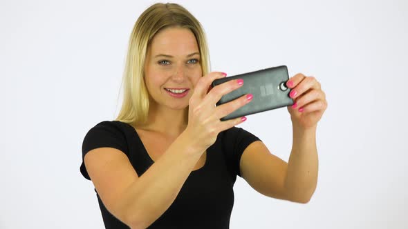 A Young Beautiful Woman Takes Pictures with a Smartphone - White Screen Studio