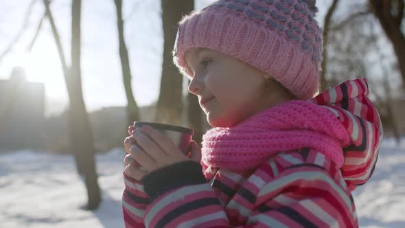 Smiling Child Kid Girl Drinking Hot Drink Tea From Cup Trying to Keep Warm in Winter Park Forest