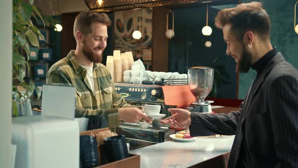 Handsome male barista gives coffee to a Man. Man buys coffee in a coffee shop.