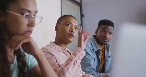 Three diverse male and female creative colleagues listening and asking questions at meeting