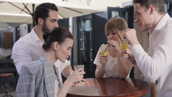 Young People Drinking Cocktails At City Street Cafe