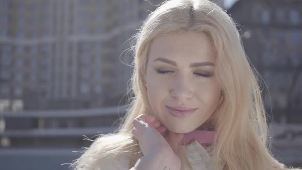 Portrait of Pretty Blond Woman Running Hand Through Her Hair and Looking in Camera Smiling. Urban