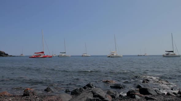 Catamarans parked in the sea, near a rocky beach. Dark black volcanic rocks in the foreground.