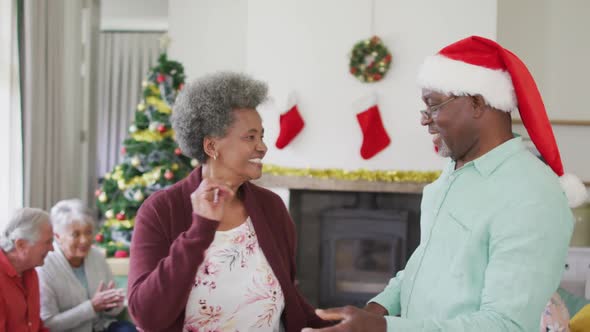 Happy african american senior couple dancing together with friends in background at christmas time