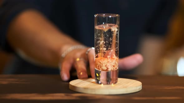 The bartender pushes forward a glass with a ready drink: baileys in sambuca.