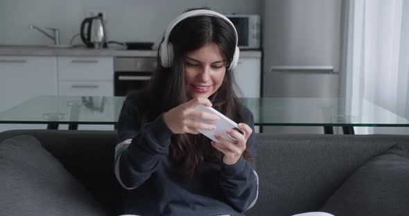 Young Brunette Girl in White Headphone Having Fun Playing Phone