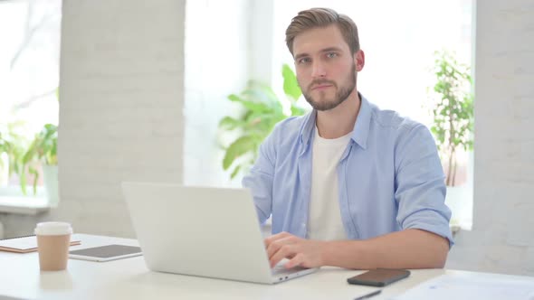 Young Creative Man with Laptop Smiling at Camera