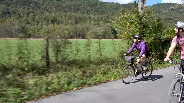 Mother and teenage son biking side by side on a rural road with farmland in the background.