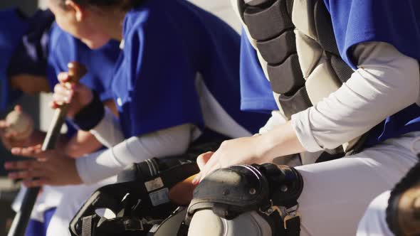 Caucasian female baseball player sitting on bench with team, putting on helmet