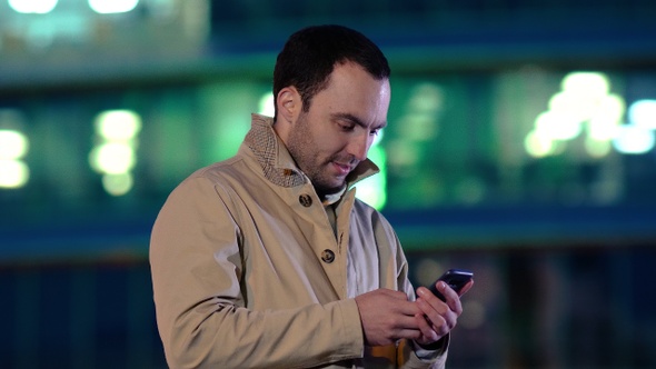Handsome adult man sending a text message while standing