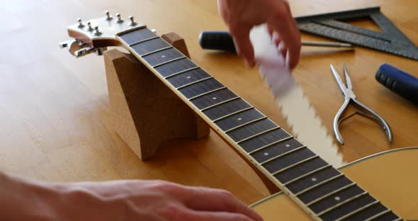 Hands of a luthier craftsman measuring and leveling an acoustic guitar neck and fretboard on a wood