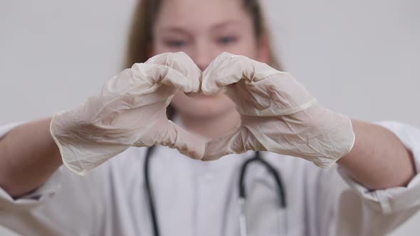 Closeup Little Female Hands in Medical Gloves Showing Heart Shape with Blurred Smiling Pretty Kid