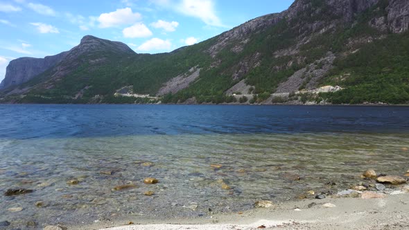 View of Norwegian fjord beach in the mountains. Sandy/rocky shore with nice weather.