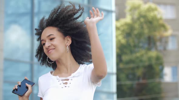 Happy Joyful Young Afro American Millennial Woman Enjoys Jumping High, Waving Arms and Dancing in