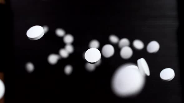 Round white pills on a black background. Super slow motion. Macro