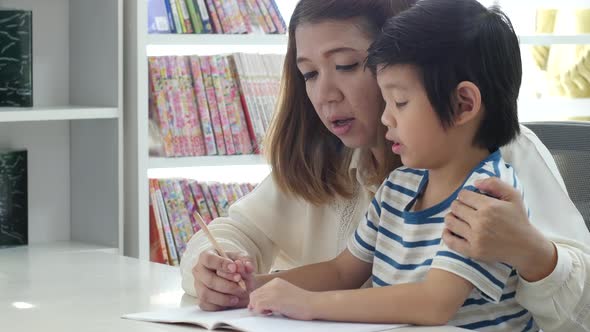 Asian Mother Helping Her Son Doing Homework On White Table