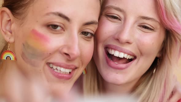 A close-up view of a smiling women are taking selfie photo using phone while kissing each other enjo