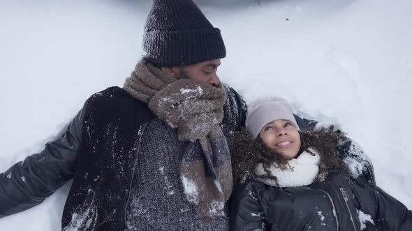 Carefree Laughing African American Man and Teen Girl Lying in White Snow Outdoors