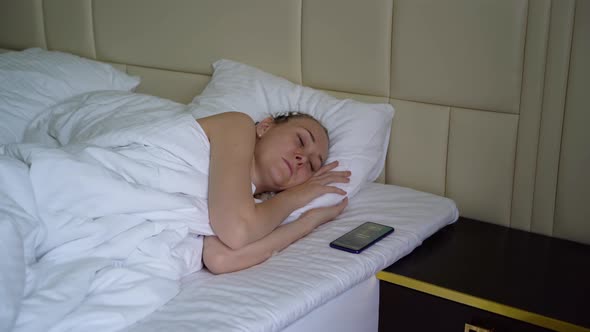 Beautiful woman with blond hair wakes up when the alarm goes off on her phone.