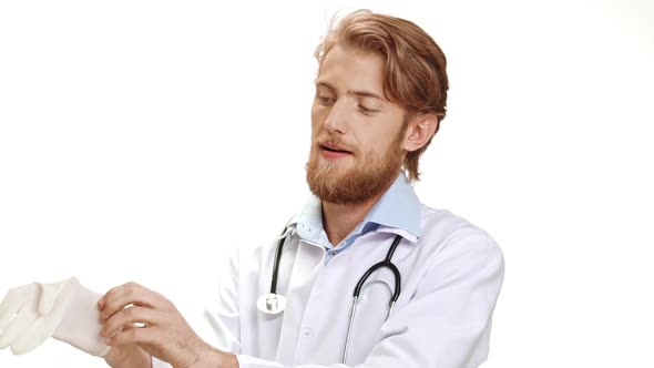 Young Caucasian Male Doctor with Light Beard and Medical Overall Smiling Wearing Disposable Latex