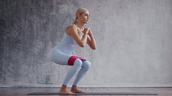 Young and sporty girl in sportswear is doing exercises in home interior using resistance band.