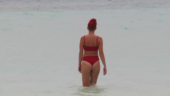 Young Woman in a Red Swimsuit Walks Into the Turquoise Ocean on Paradise Beach