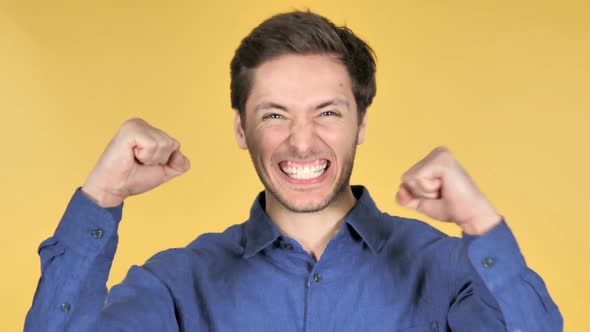 Casual Young Man Celebrating Success on Yellow Background