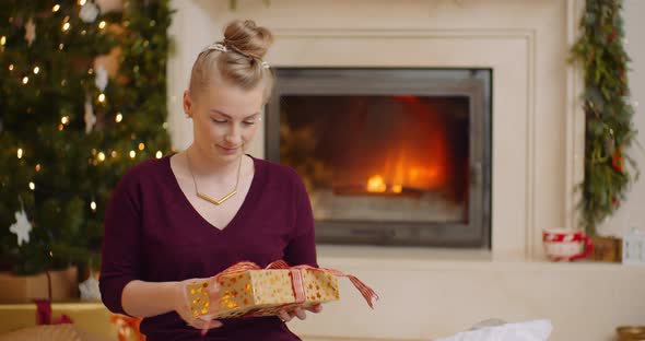 Young Woman Holding Christmas Present Against Fireplace