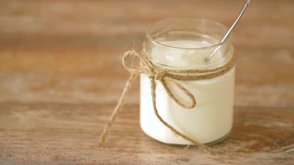 Yogurt or Sour Cream in Glass Jar on Wooden Table