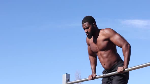 Strong black sportsman working out on bar in town