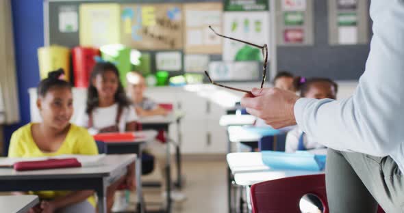 Midsection of diverse male teacher conducting lesson in classroom with children