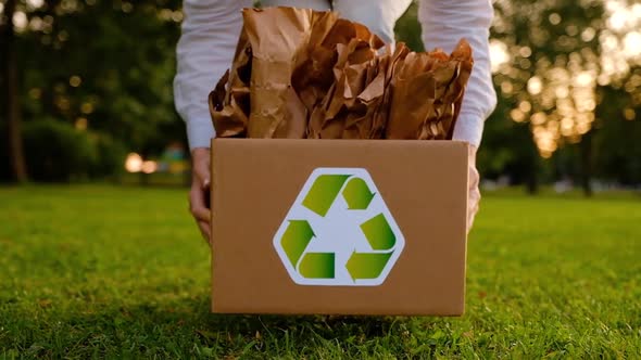 Young woman holds a box with paper bags with a recyclable raw material icon